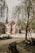A whimsical, fairytale-style cottage with a curved, shingled roof and wooden accents nestled among trees. The scene is rustic and serene with a sandy path leading to the house. A small tree stump and foliage can be seen in the foreground, adding to the natural ambiance.