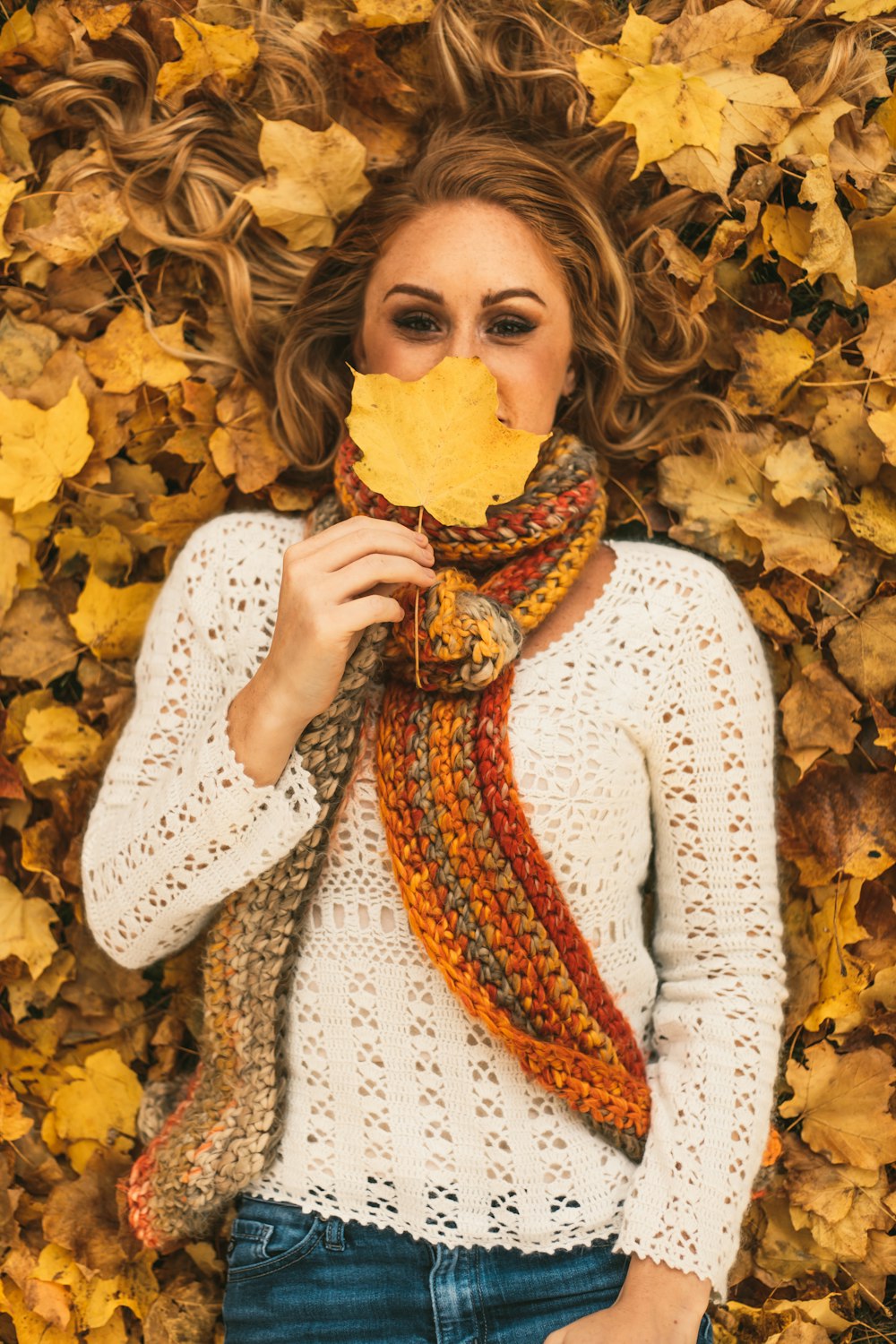 woman lying on yellow leaves covering half her face with a leaf