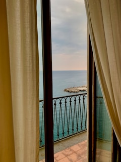 A serene beach view through a large window, with soft sunlight illuminating a wooden desk.