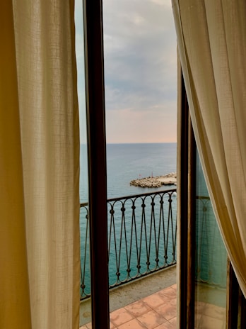 A serene beach view through a large window, with soft sunlight illuminating a wooden desk.
