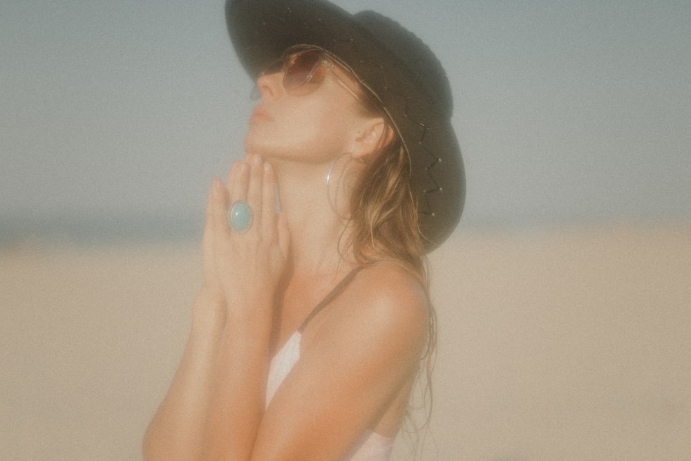 a woman wearing a hat and sunglasses standing in the sand