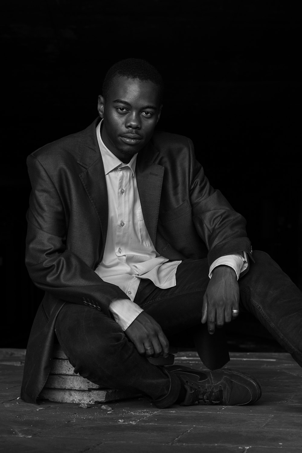 grayscale photo of man sitting on concrete ground