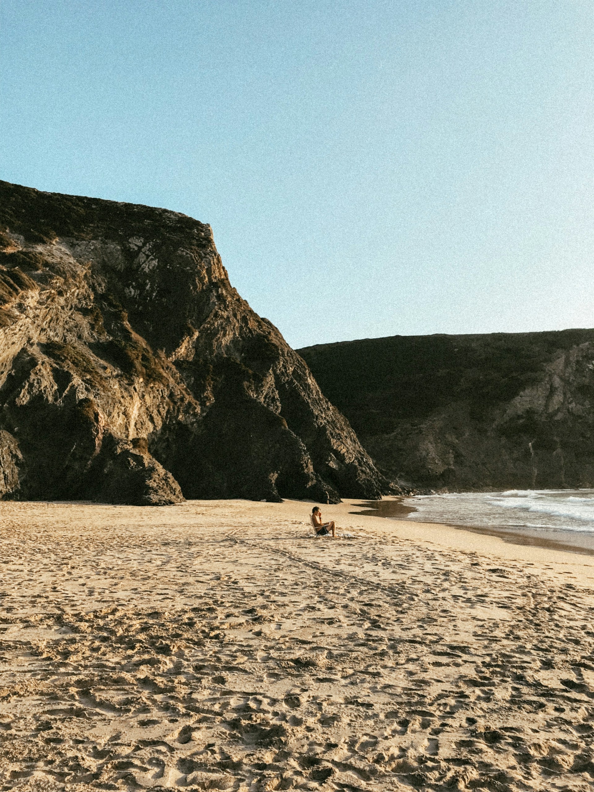 A peaceful beach scene with a lone traveler sitting on the sand, gazing out at the endless ocean horizon.