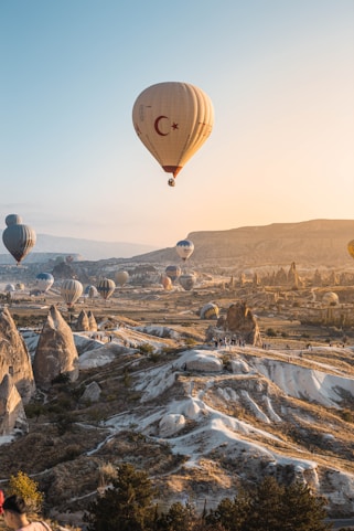 A vibrant sunrise over Cappadocia with colorful hot air balloons ascending above fairy chimneys.