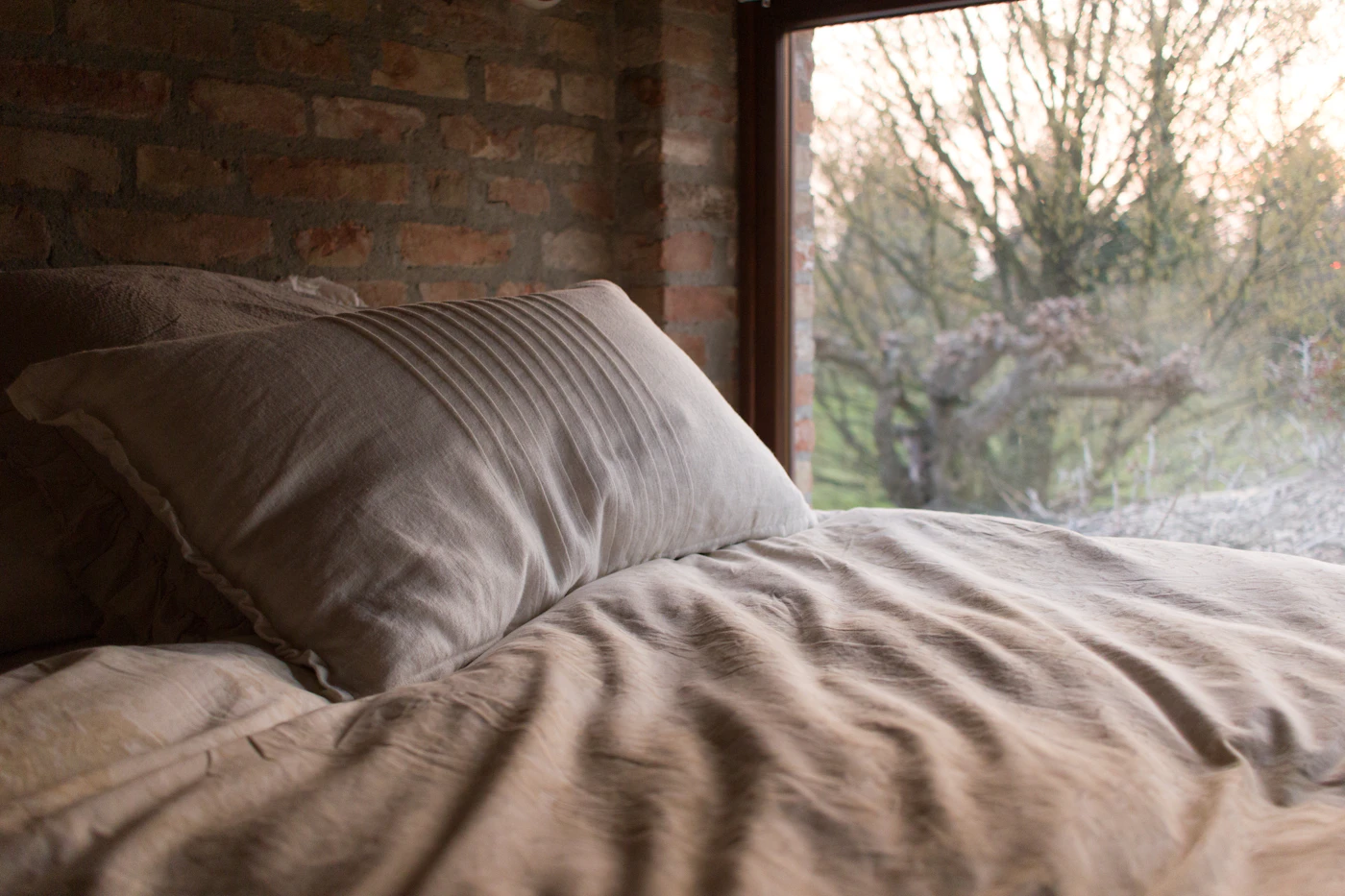 Washed linen bedding against an old brick wall beside a garden window