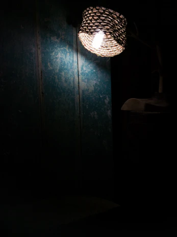The gentle glow of a woven wall lamp highlighting textured plaster walls in a serene living room.