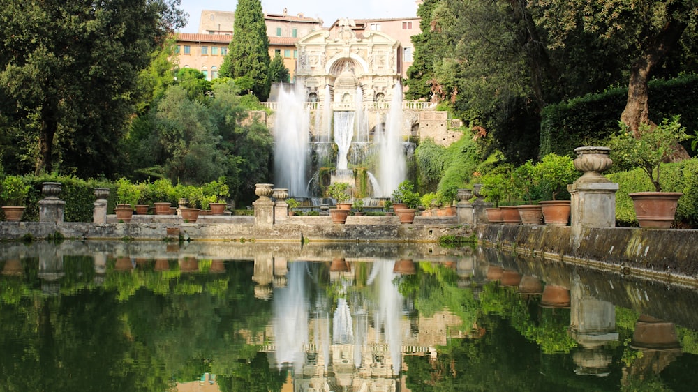 Gewässer in der Nähe des Wasserbrunnens im Freien, umgeben von hohen und grünen Bäumen, die tagsüber das Schloss betrachten