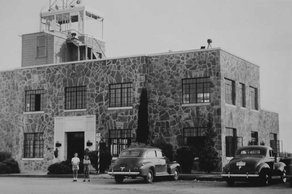 grayscale photography of two cars parked outside a building