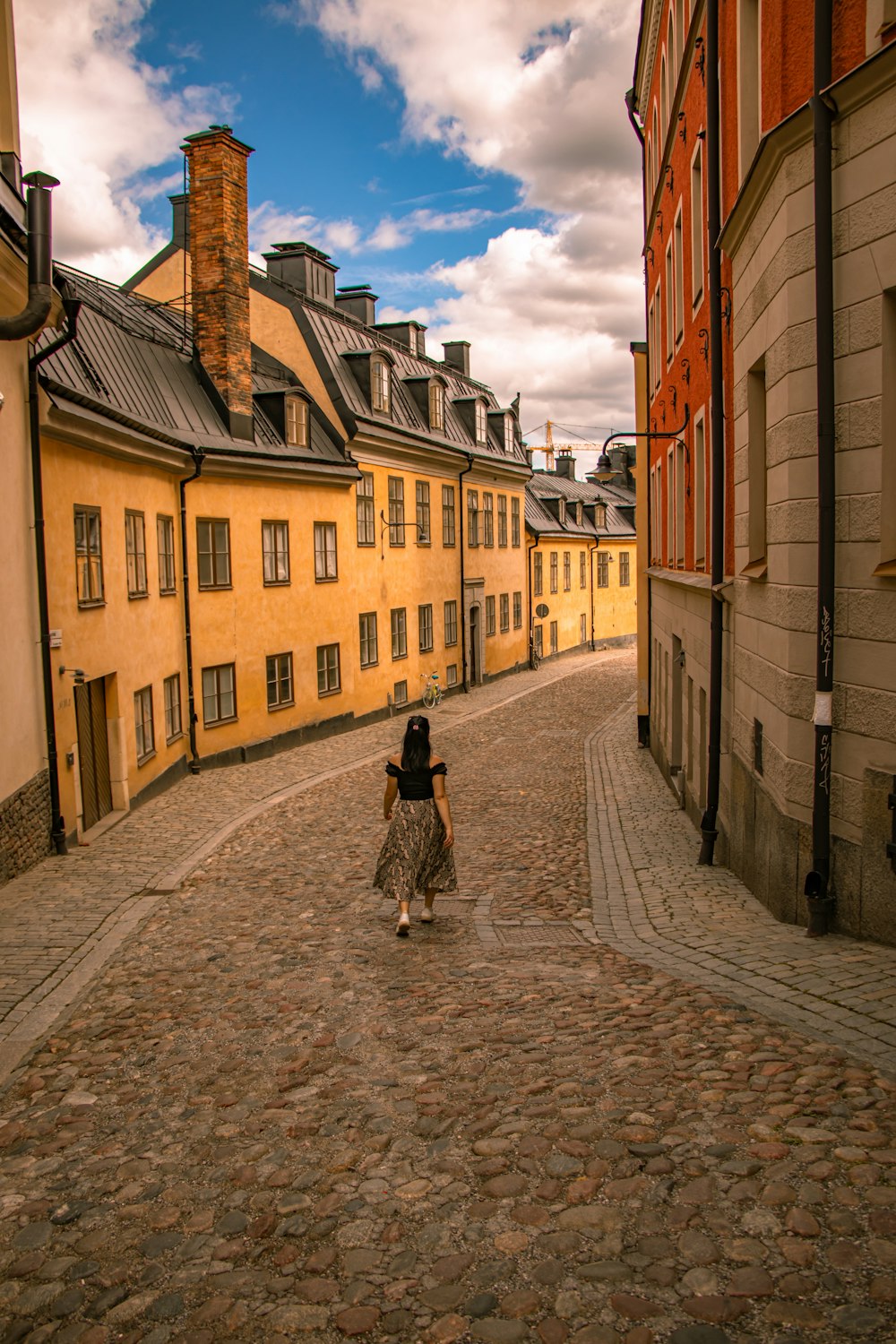 woman walking on concrete road in between buildings under white and blue skies during daytime