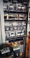 An electrical switchgear panel with multiple circuit breakers and wiring is organized within a metal frame. Colored wires are neatly attached, and labels or indicators can be seen on some components. The environment suggests an industrial or technical setting.