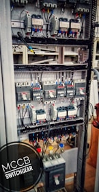 An electrical switchgear panel with multiple circuit breakers and wiring is organized within a metal frame. Colored wires are neatly attached, and labels or indicators can be seen on some components. The environment suggests an industrial or technical setting.