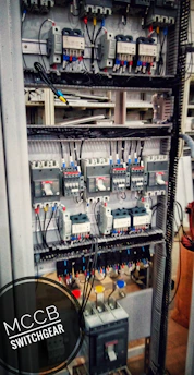 Electrician wiring a modern switchgear panel with LED lighting overhead.