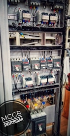 An electrical switchgear panel with multiple circuit breakers and wiring is organized within a metal frame. Colored wires are neatly attached, and labels or indicators can be seen on some components. The environment suggests an industrial or technical setting.