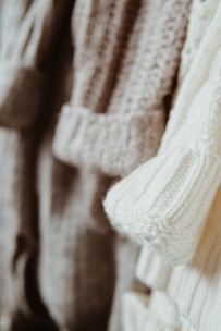 Close-up of soft sweaters and cardigans in warm, earthy tones displayed on wooden hangers.