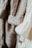 Close-up view of several knitted sweaters in soft, neutral tones hanging together. The textures of the various knit patterns are clearly visible, showcasing different stitch types and detailing.