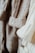 Close-up view of several knitted sweaters in soft, neutral tones hanging together. The textures of the various knit patterns are clearly visible, showcasing different stitch types and detailing.