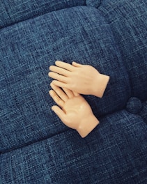 Two small plastic hands resting on a textured blue fabric surface, resembling a couch or cushion.