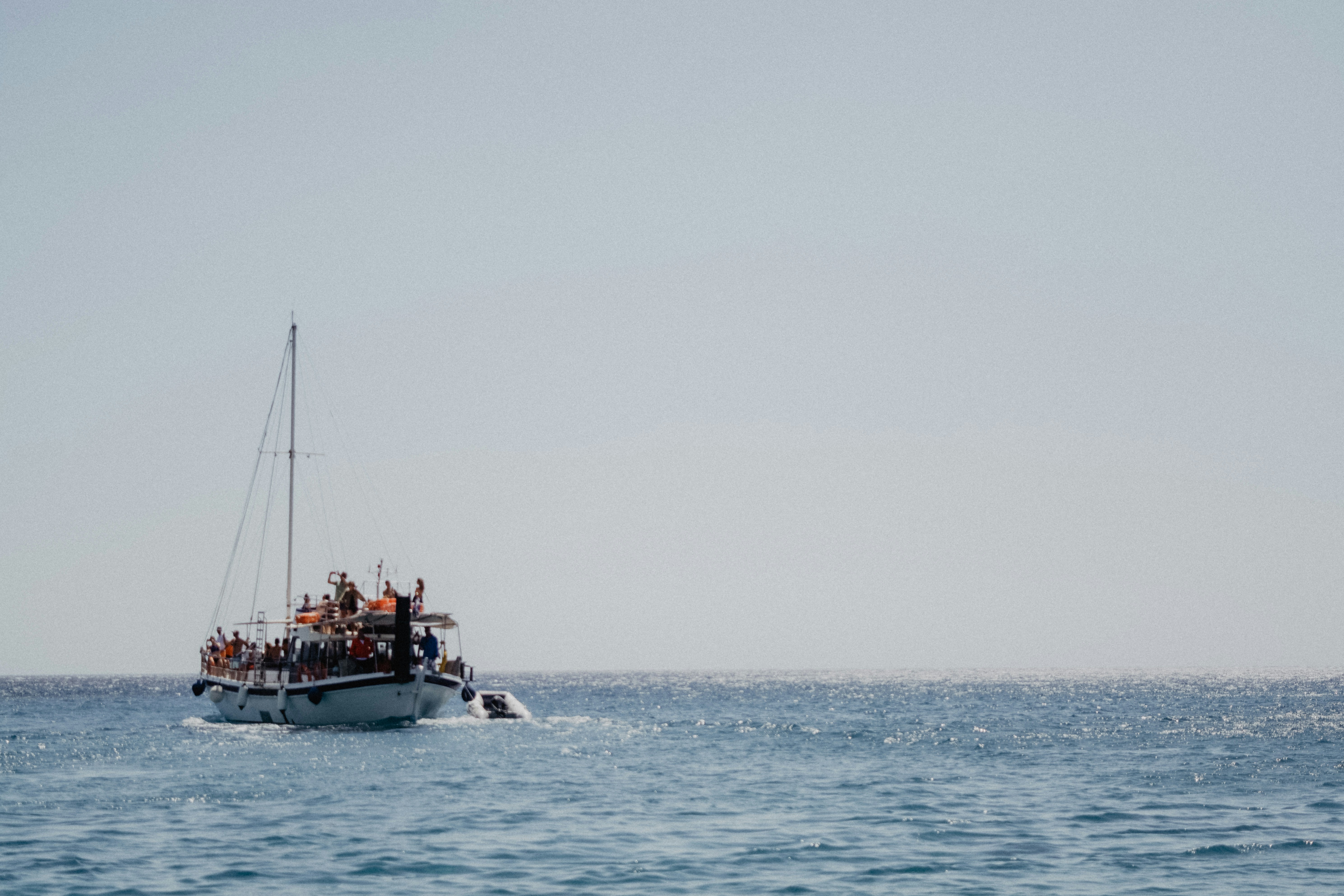 Passenger boat sailing on open water under a clear sky, with people gathered on deck in the distance.