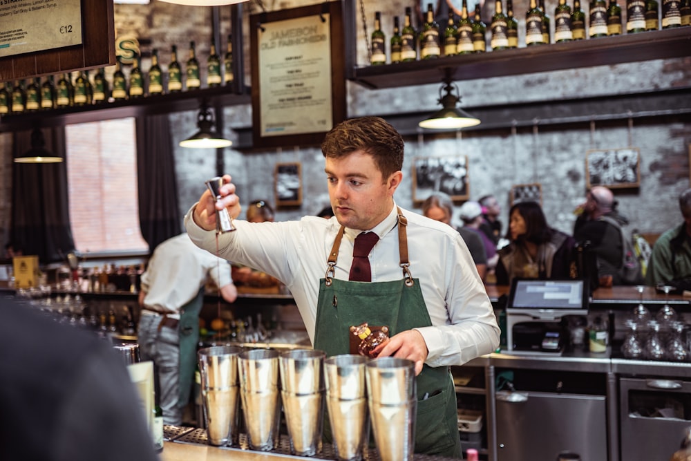 shallow focus photo of man pouring liquid on stainless steel cups