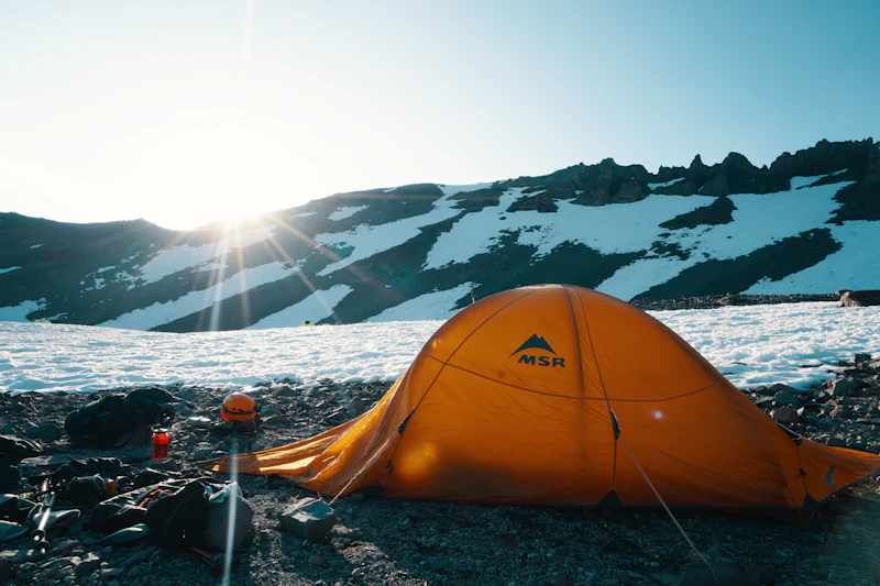 Freestanding orange dome tent pitched below alpine peaks