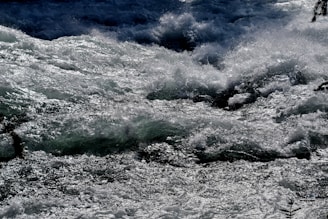 Turbulent water flows rapidly, creating a dynamic and powerful scene with waves and splashes catching the light.