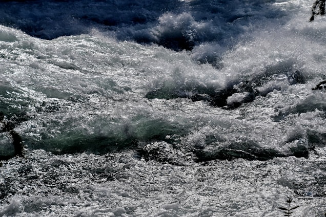 Turbulent water flows rapidly, creating a dynamic and powerful scene with waves and splashes catching the light.