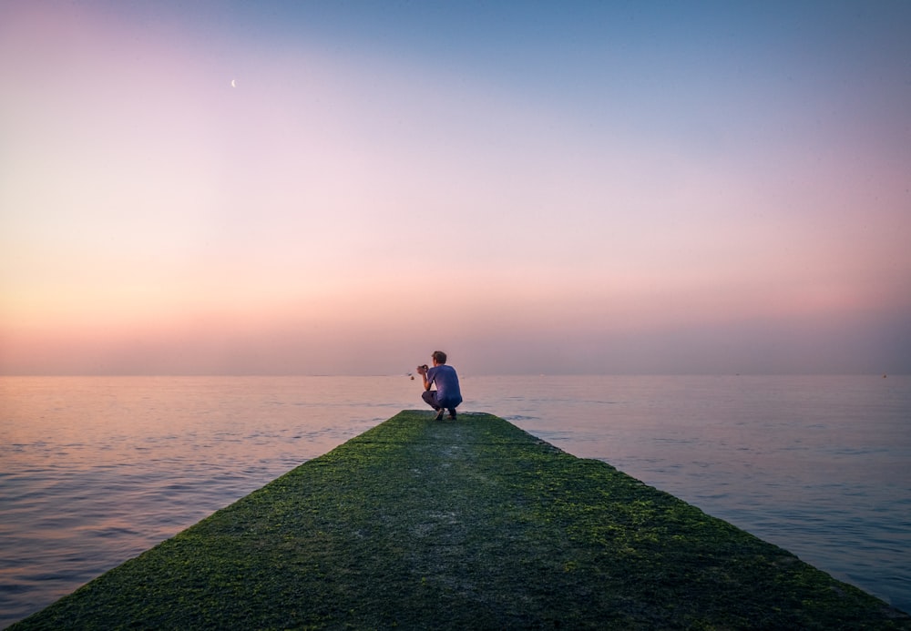 man sitting beside body of water