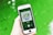 A hand is holding a smartphone displaying a music app with album art and music controls visible on the screen. The background consists of a vibrant green surface.