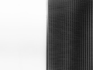 A solar panel with a sleek design is split into two halves. The left side is a clean white surface, while the right side features a pattern of dark vertical lines representing the photovoltaic cells.