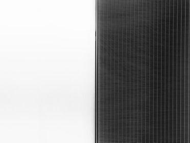 A solar panel with a sleek design is split into two halves. The left side is a clean white surface, while the right side features a pattern of dark vertical lines representing the photovoltaic cells.