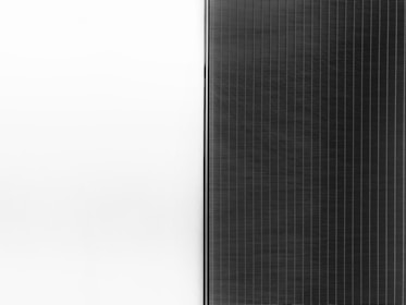 A solar panel with a sleek design is split into two halves. The left side is a clean white surface, while the right side features a pattern of dark vertical lines representing the photovoltaic cells.