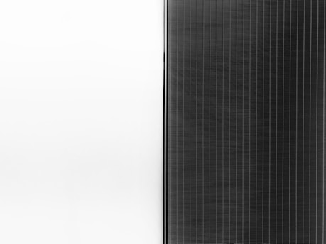 A solar panel with a sleek design is split into two halves. The left side is a clean white surface, while the right side features a pattern of dark vertical lines representing the photovoltaic cells.