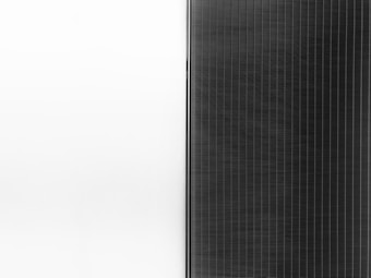 A solar panel with a sleek design is split into two halves. The left side is a clean white surface, while the right side features a pattern of dark vertical lines representing the photovoltaic cells.