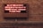 A neon sign is displayed on a brick wall, reading 'ALL OF THE ELECTRICITY NOW IN USE IN THIS FACILITY OF ARGONNE NATIONAL LABORATORY IS ATOMIC POWER'. The sign emits a reddish glow, contrasting with the earthy tones of the brick wall background.
