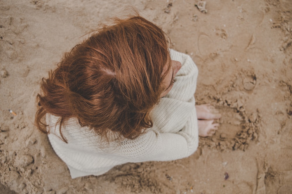 a woman with red hair is sitting in the sand