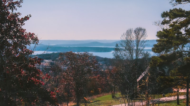 Morning fog lifting off Table Rock Lake, seen through red and orange autumn trees with layered Ozark ridges behind