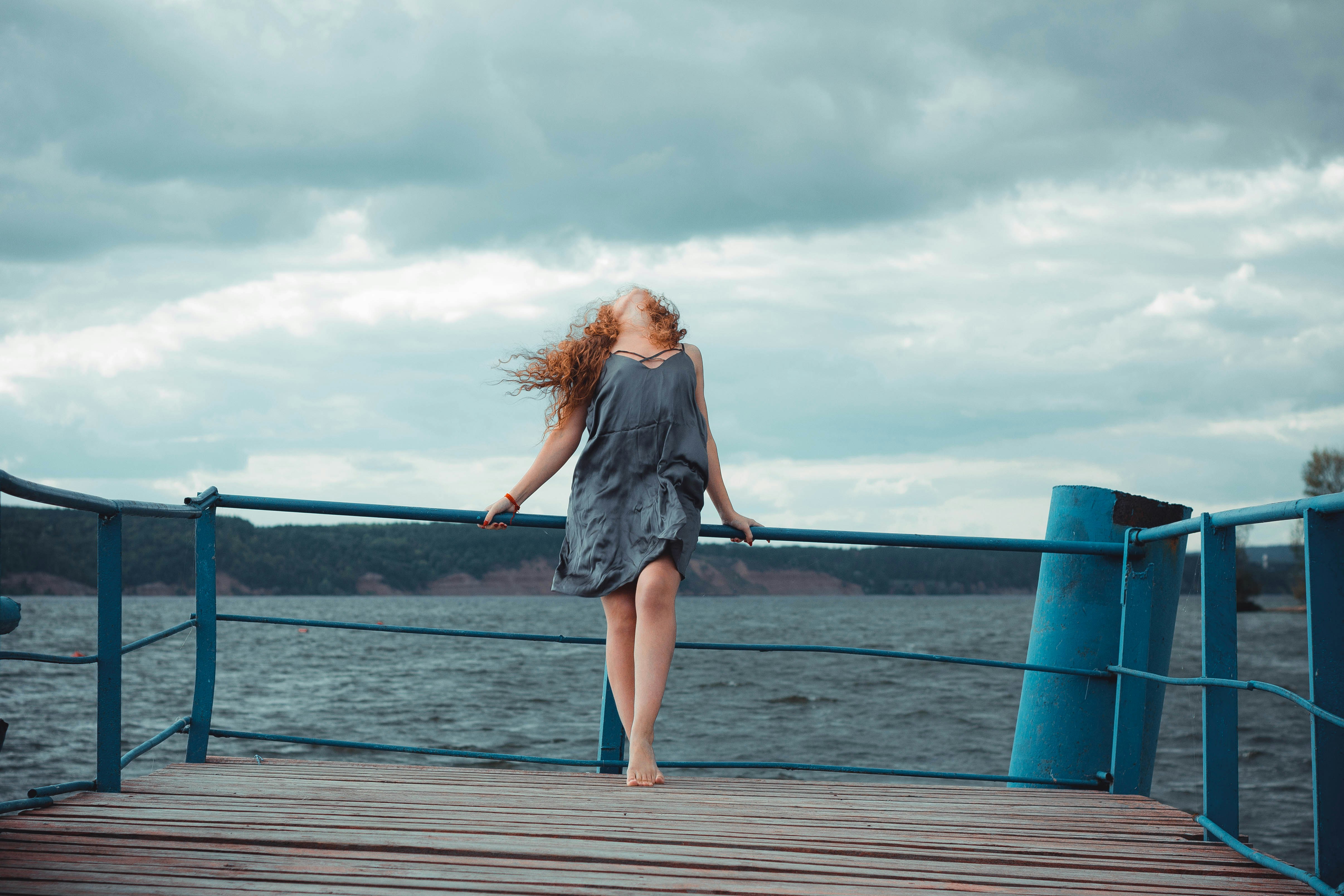 woman standing on dock and bending her body during daytime, 