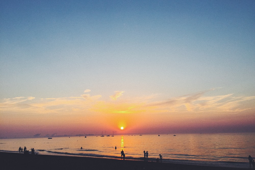 people gathering beside seashore during sunset