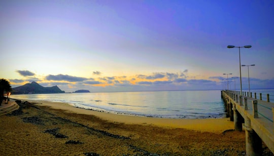 brown sand, blue body of water, and brown wooden dock in Porto Santo Portugal