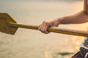 Close-up of hands gripping a paddle cutting through calm, sparkling water.