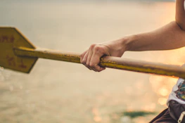 Close-up of hands gripping a paddle cutting through calm, sparkling water.