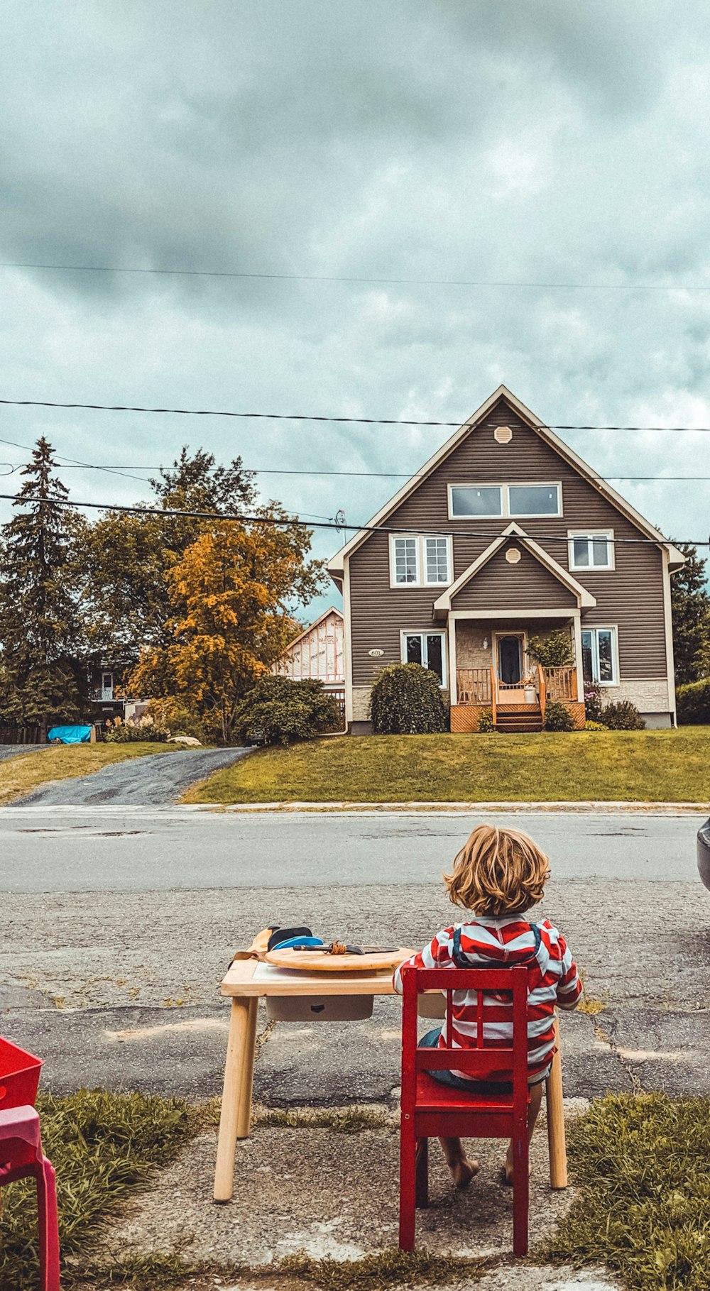 boy sitting on red chair facing near house