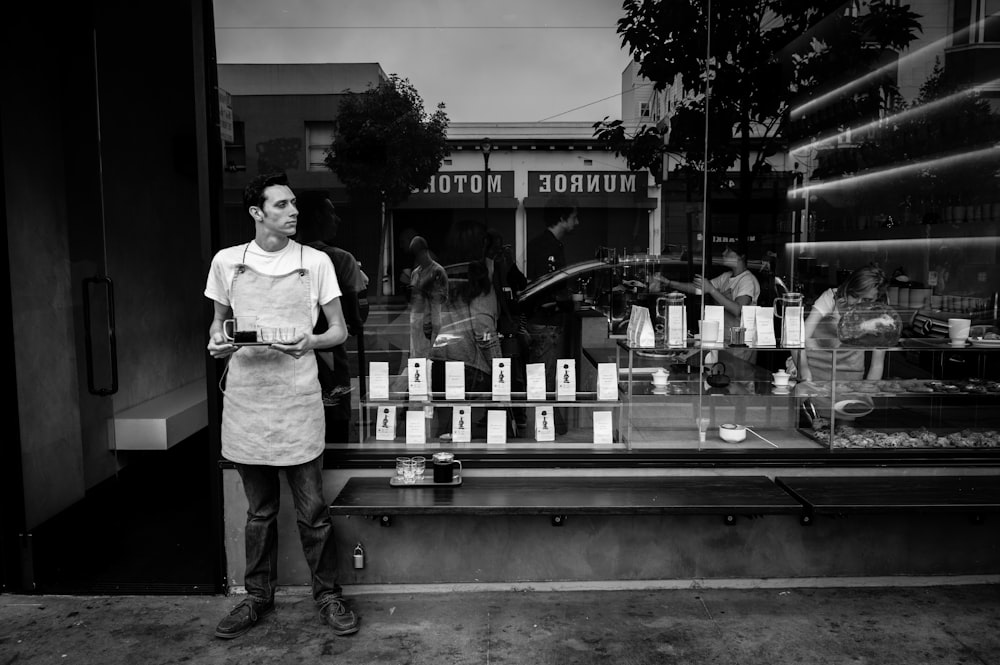 grayscale photography of man standing near glass wall