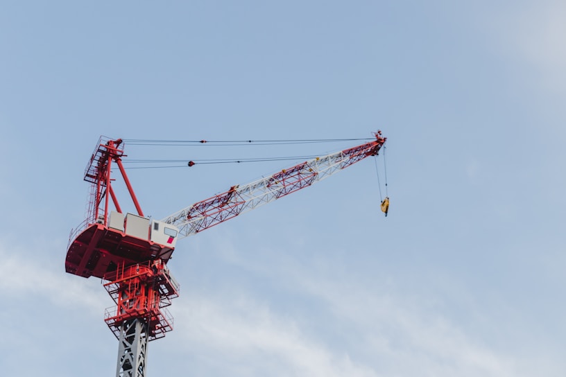 A powerful crane lifting heavy steel beams at a busy construction site under a clear blue sky.
