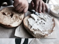 A smiling customer enjoying a bagel with cream cheese at a small café table.
