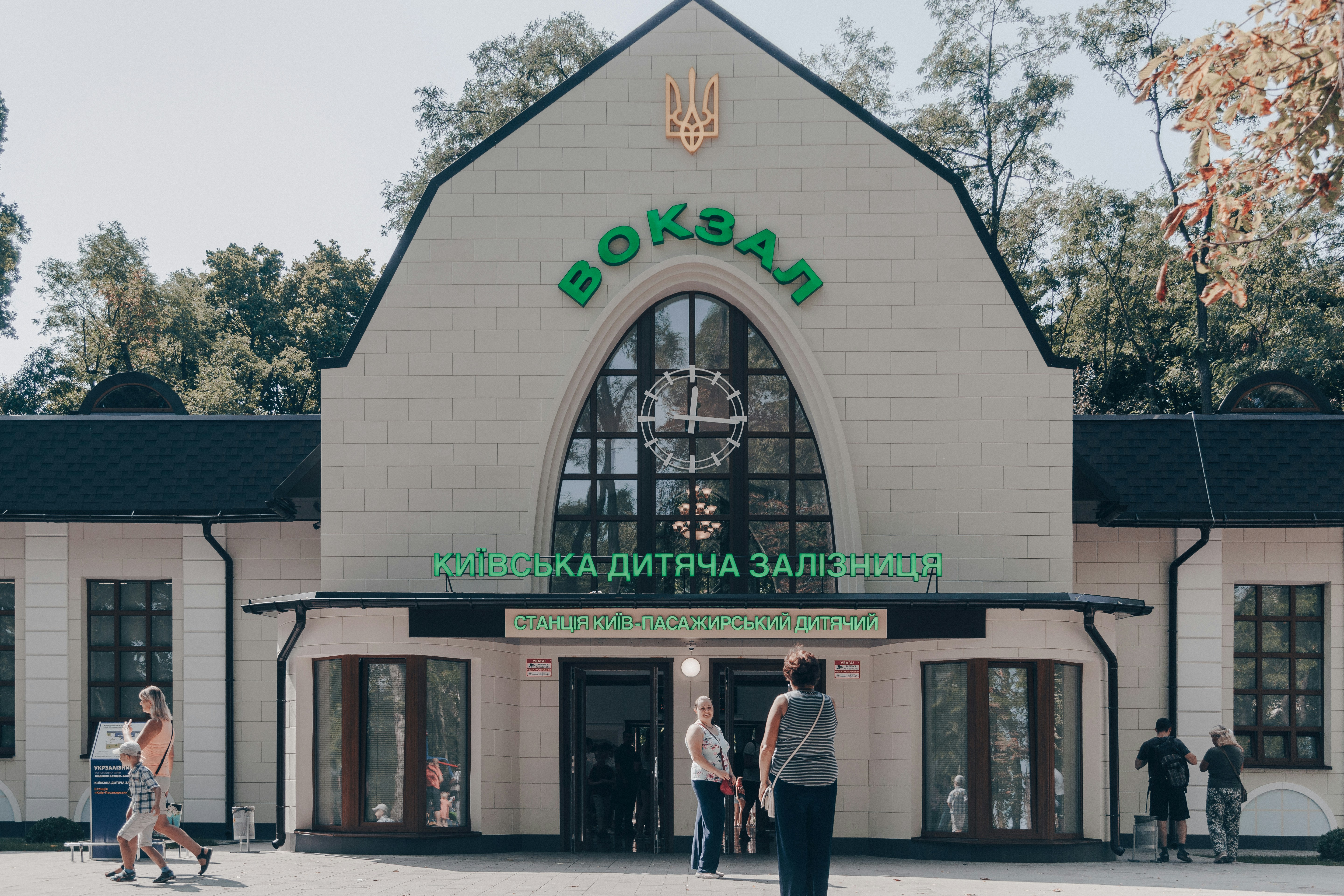 people walking near white and black building surrounded with tall and green trees during daytime