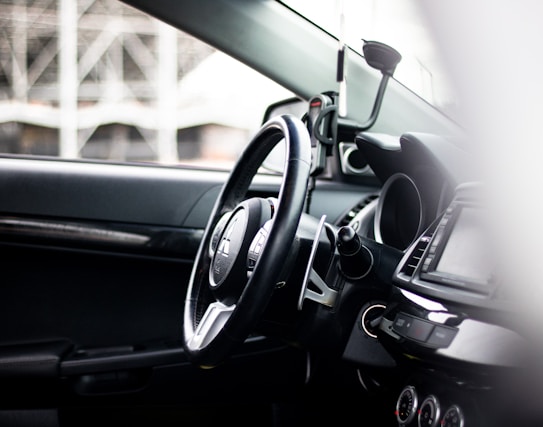 The interior of a car, focusing on the steering wheel and dashboard area with visible controls and gauges. A phone holder is mounted on the dashboard, and the overall view suggests a modern and clean vehicle interior.