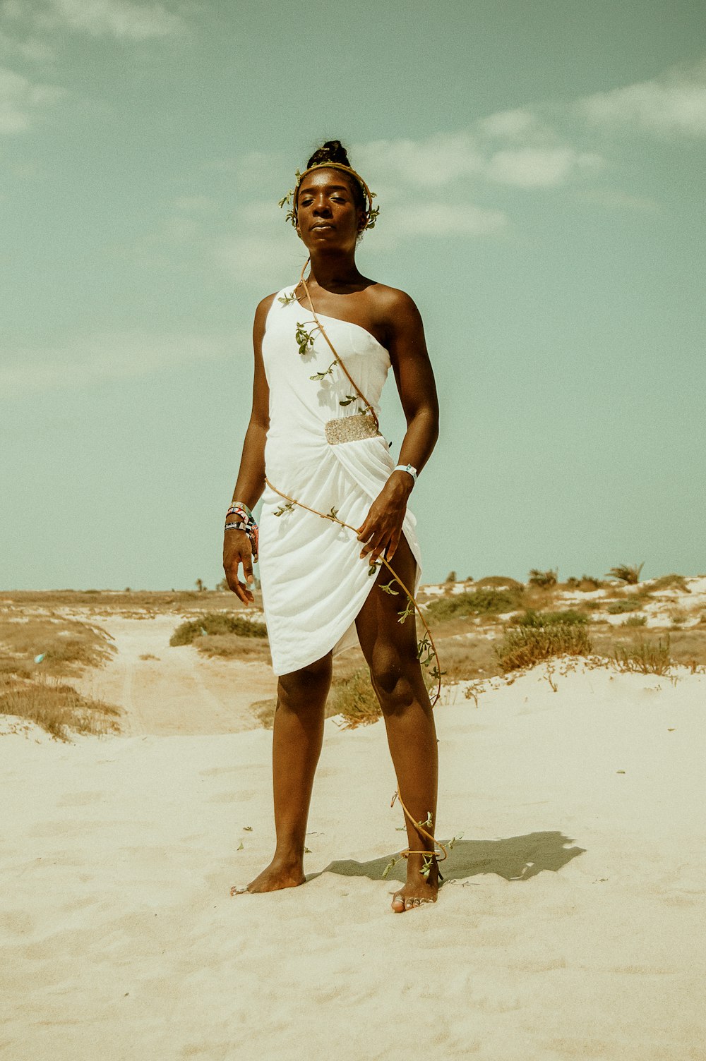 Mujer con vestido blanco de un solo hombro de pie sobre la arena