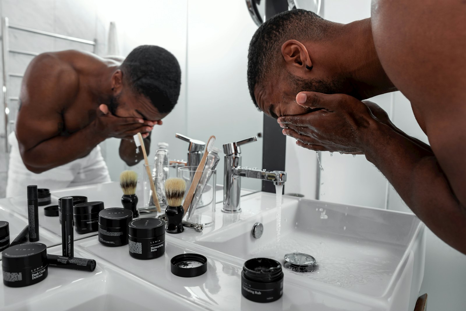 Man washing his face at a bathroom sink with grooming products