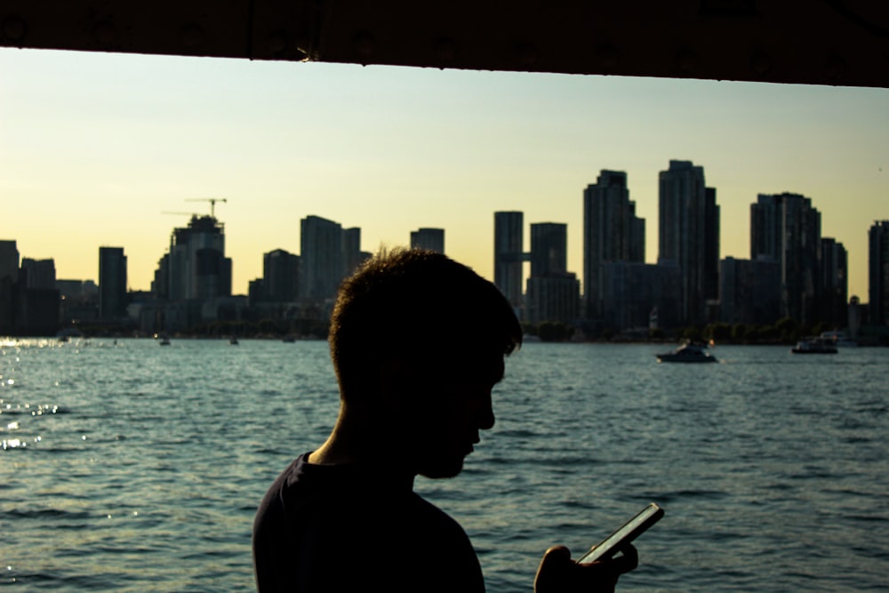 a man standing in front of a body of water holding a cell phone